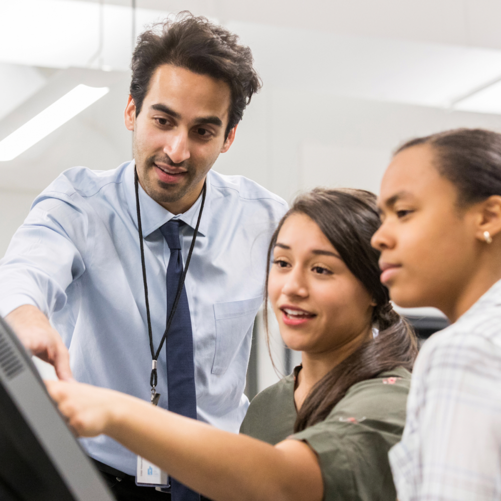 A lab instructor helps two students with their project. 