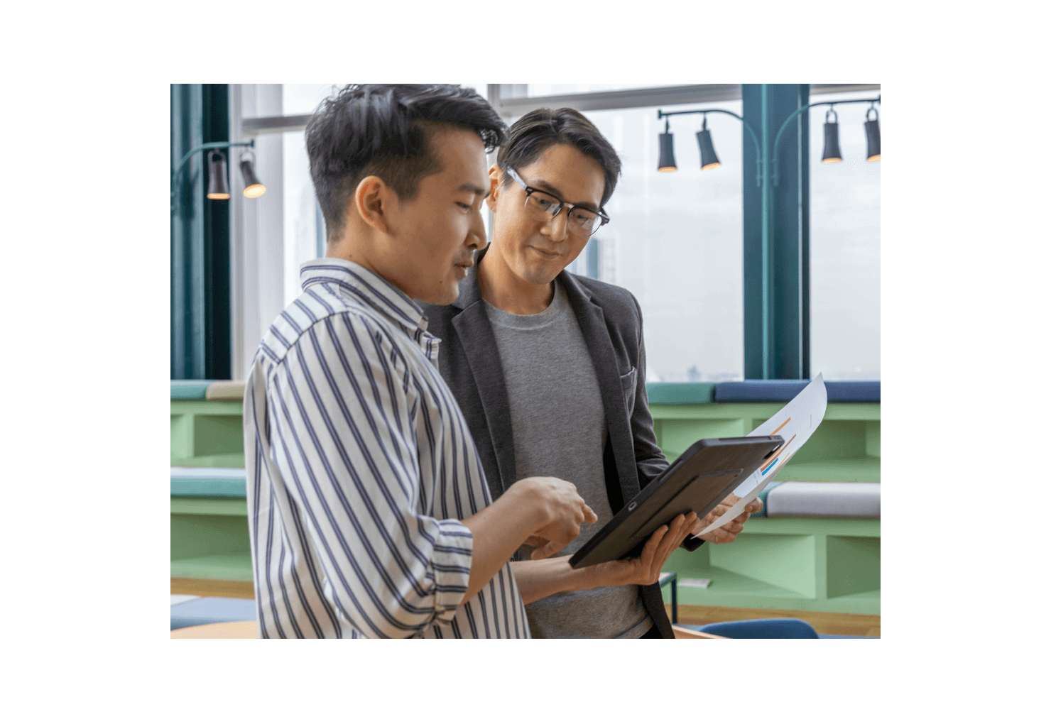 Two men look at a tablet and review a document together. 
